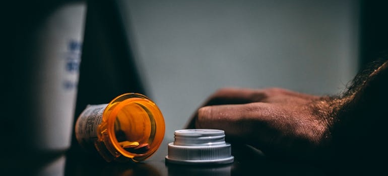 Man's hand next to a spilled bottle of pills.