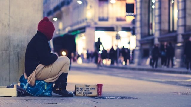 Photo of a homeless person looking towards a group of people as a featured image for post about homelessness and substance abuse