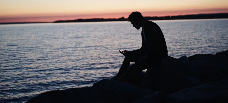 A man sitting on the beach and looking at a phone.