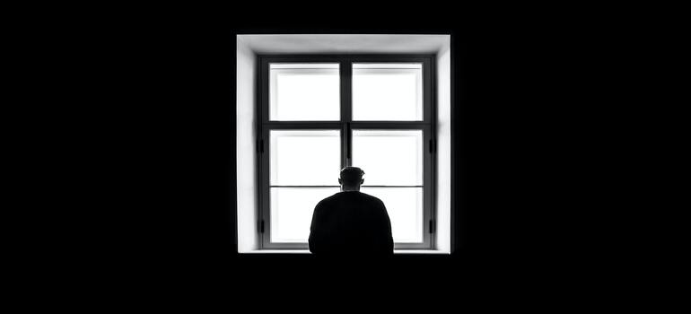 Person suffering of addiction standing in the dark and looking out a window.