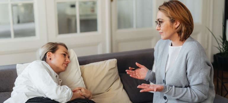 Two women having a serious conversation about eating disorders and substance abuse while sitting on a couch.