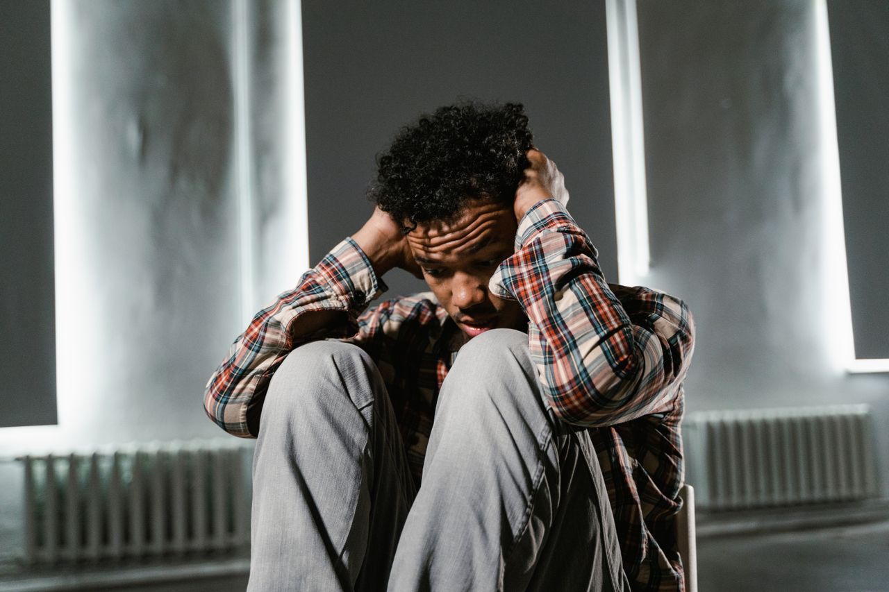 Anxious adult man sitting alone on a chair with his hands on his head while worrying about drug use and panic attacks.