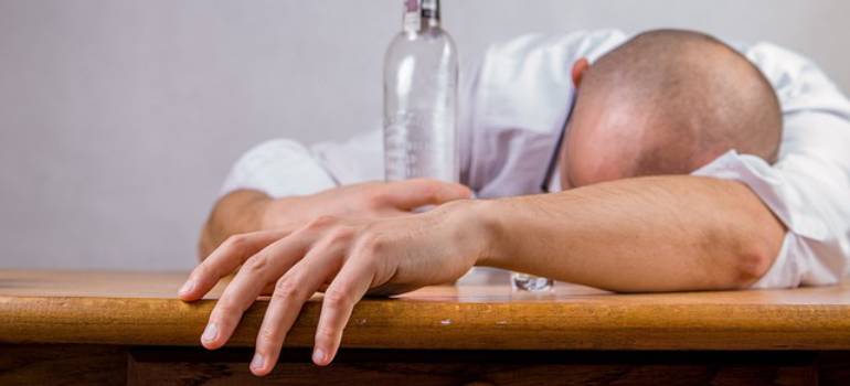 A drunk person sleeping at the table hugging a bottle.
