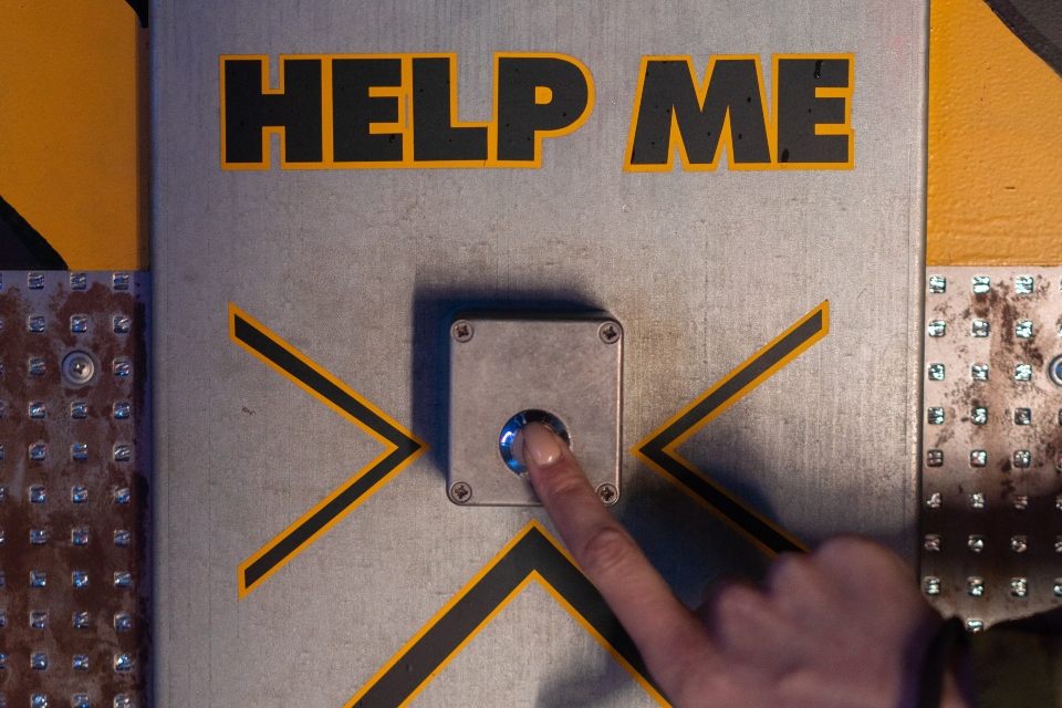 person pressing a button labeled "help me"