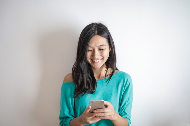 A woman smiling at her phone after seeing her results on some addiction recovery apps.
