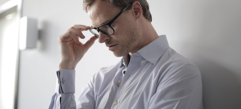 a stressed man against the wall adjusting his glasses