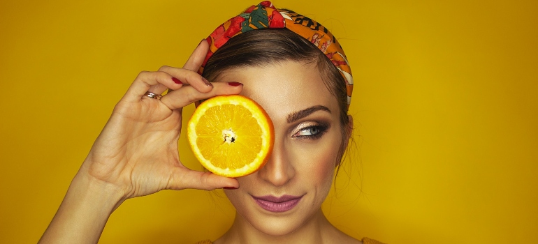 Woman covering her eye with a slice of orange