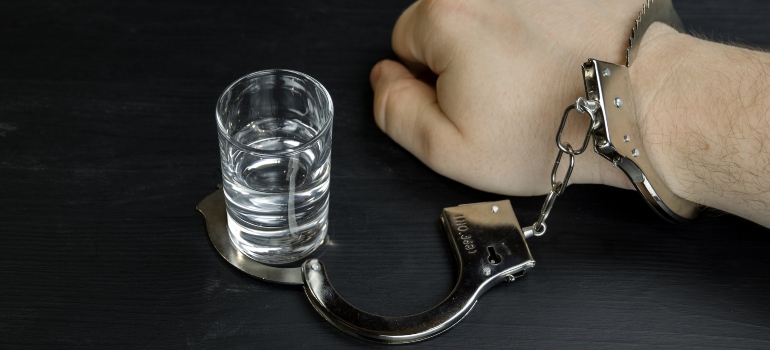 Person's hand handcuffed to a shot of alcohol to symbolize alcoholism