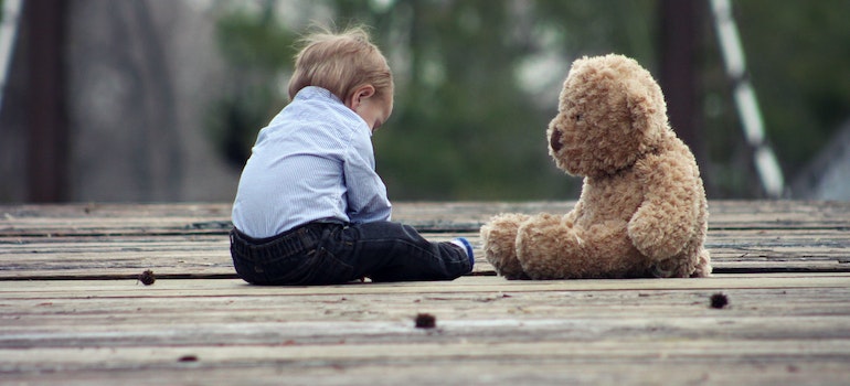 a boy sitting next to his teddy bear