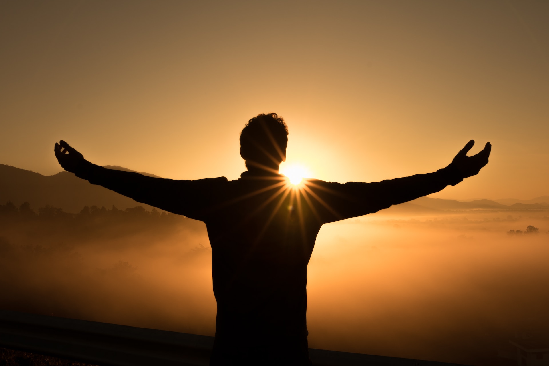 Silhouette of a person holding their hands in the air during sunrise