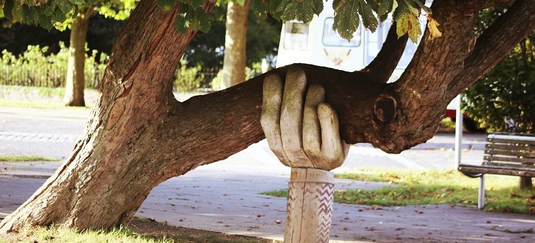 Giant hand holding a leaning tree.