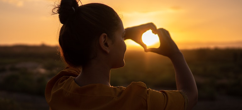 Woman making a hear with her hands in the sunset.