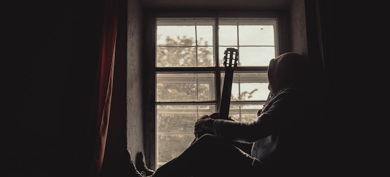 a man holding a guitar sitting on the window pane