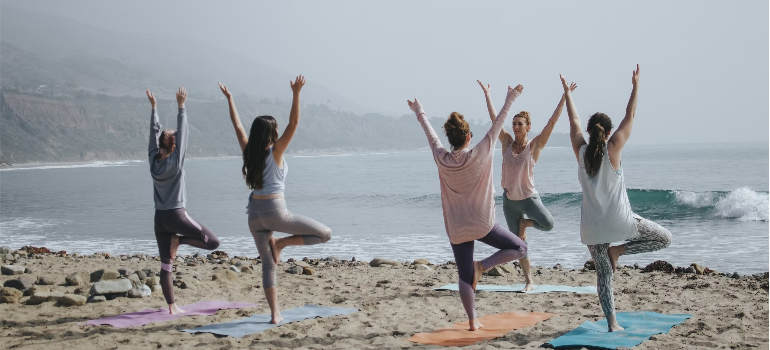 A group of women doing yoga by the sea, illustrating the impact of sports and physical activity in Pennsylvania.