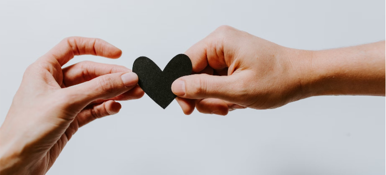 A close-up of two people sharing a papercut heart.