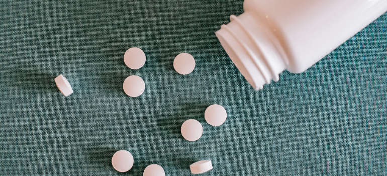 a pile with white pills and a container 