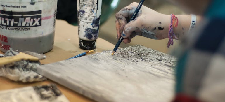 A person drawing with a black pencil with colors next to them and dirty hands