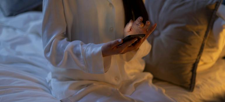 A woman in white pajamas sitting on the bed with a phone in her hands 