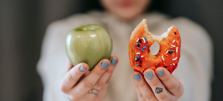 A person holing a donut and an apple. 