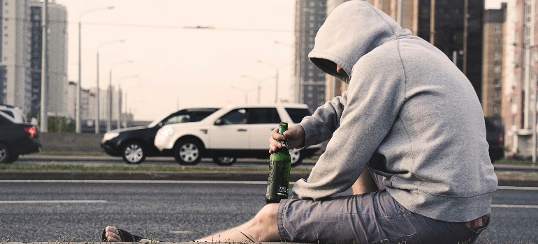 a man sitting on the street drinking a beer and wondering how long does it take alcohol to leave your system