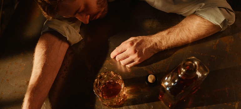 a man lying on the floor with a bottle and a glass of alcohol next to him 