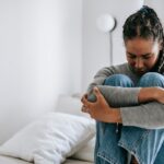 a woman experiencing methadone withdrawal symptoms embracing knees on bed