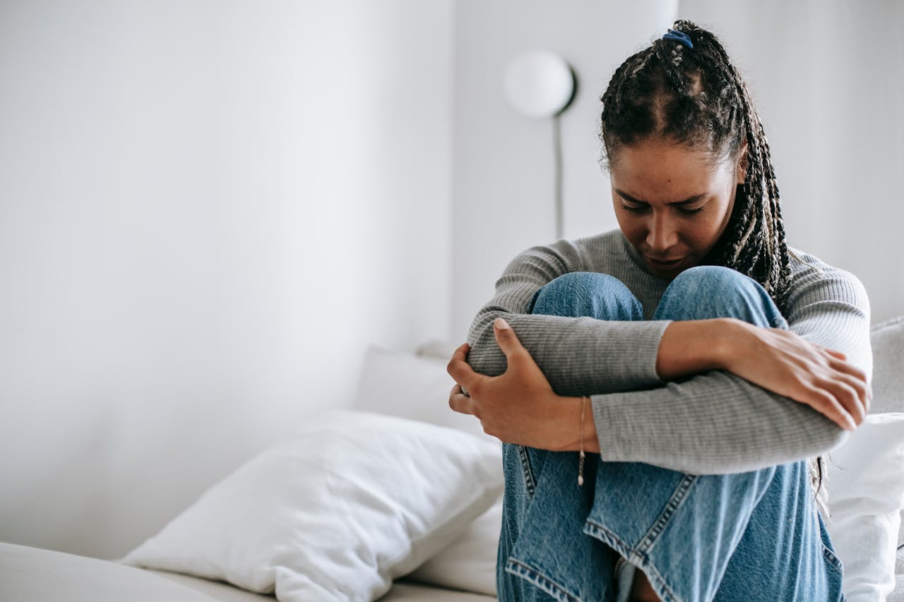 a woman experiencing methadone withdrawal symptoms embracing knees on bed