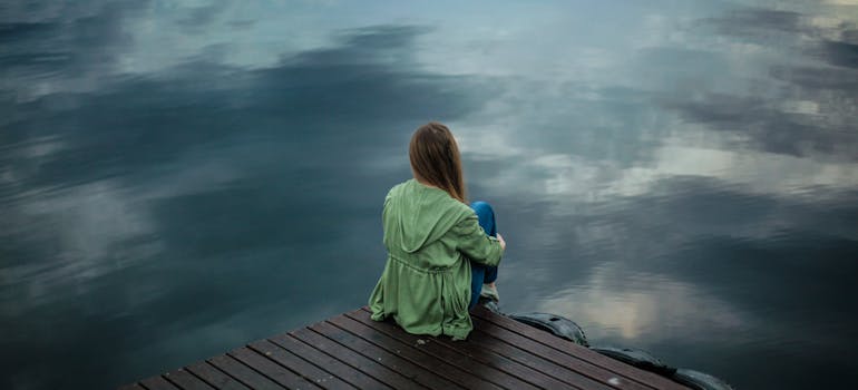 Woman sitting on the edge of a wooden board looking at a lake thinking about the dangers of heroin vs. cocaine
