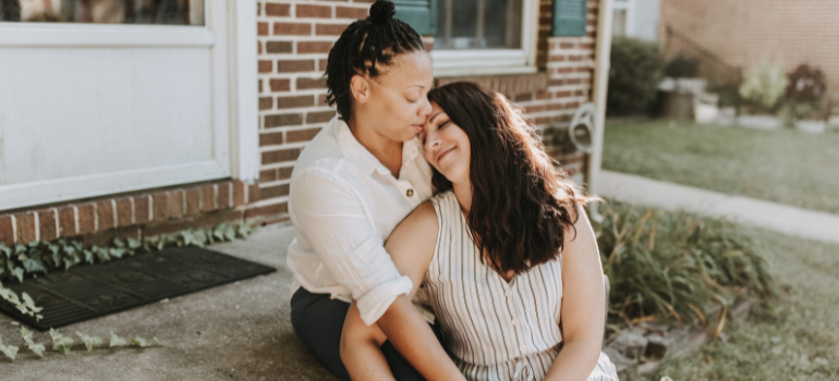 A woman of color comforts the other woman by kissing her on the forehead.
