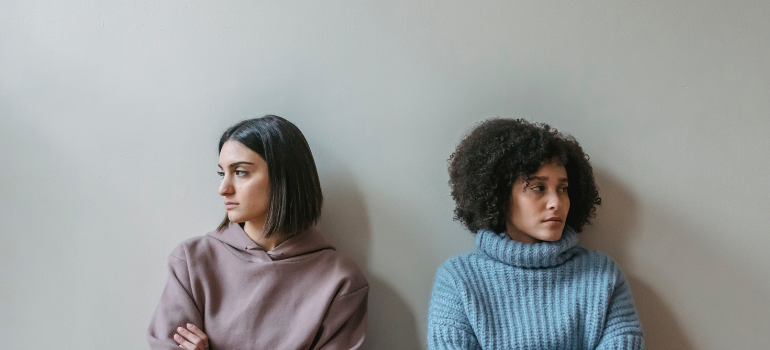 Two young women with their hair down and oversize sweaters look in opposite directions