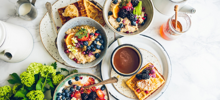 Three big bowls of yogurt with granola and fresh fruit, each with a side of waffles.