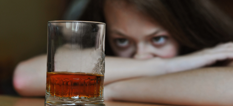 A young girl scowls at a whiskey glass in front of her