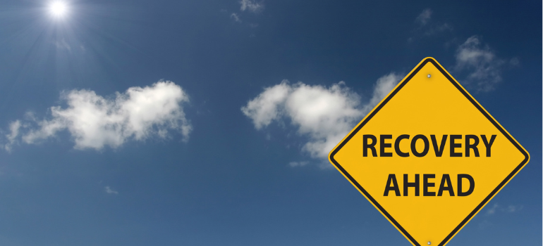 A traffic sign reading recovery ahead against a blue sky background