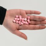 A person holding pink pills in their palm