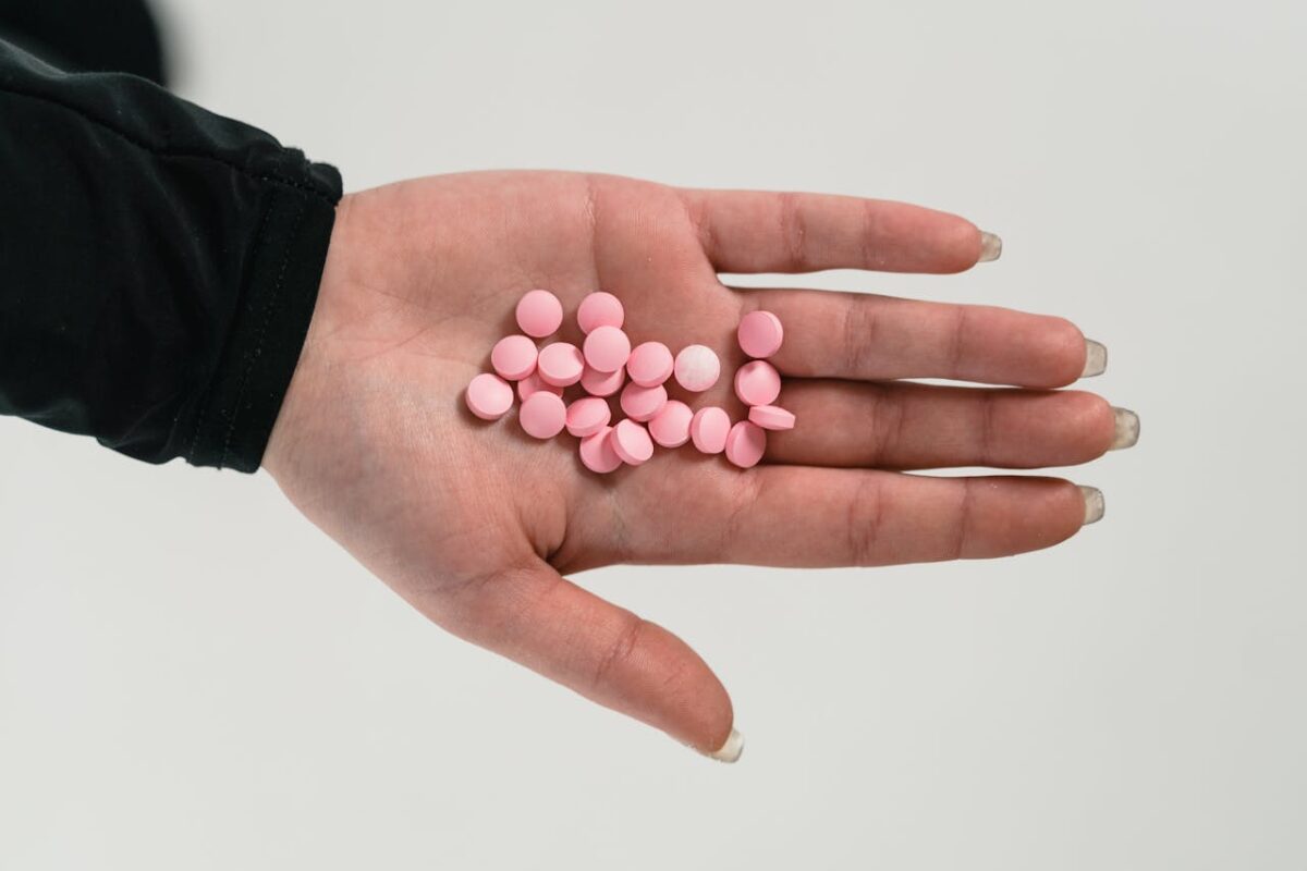 A person holding pink pills in their palm