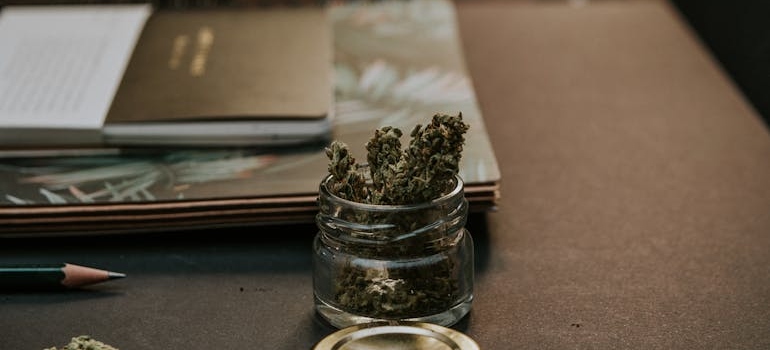 Cannabis in a jar next to a notebag.
