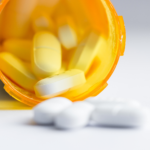 An orange bottle placed horizontally out of which white pills come out.
