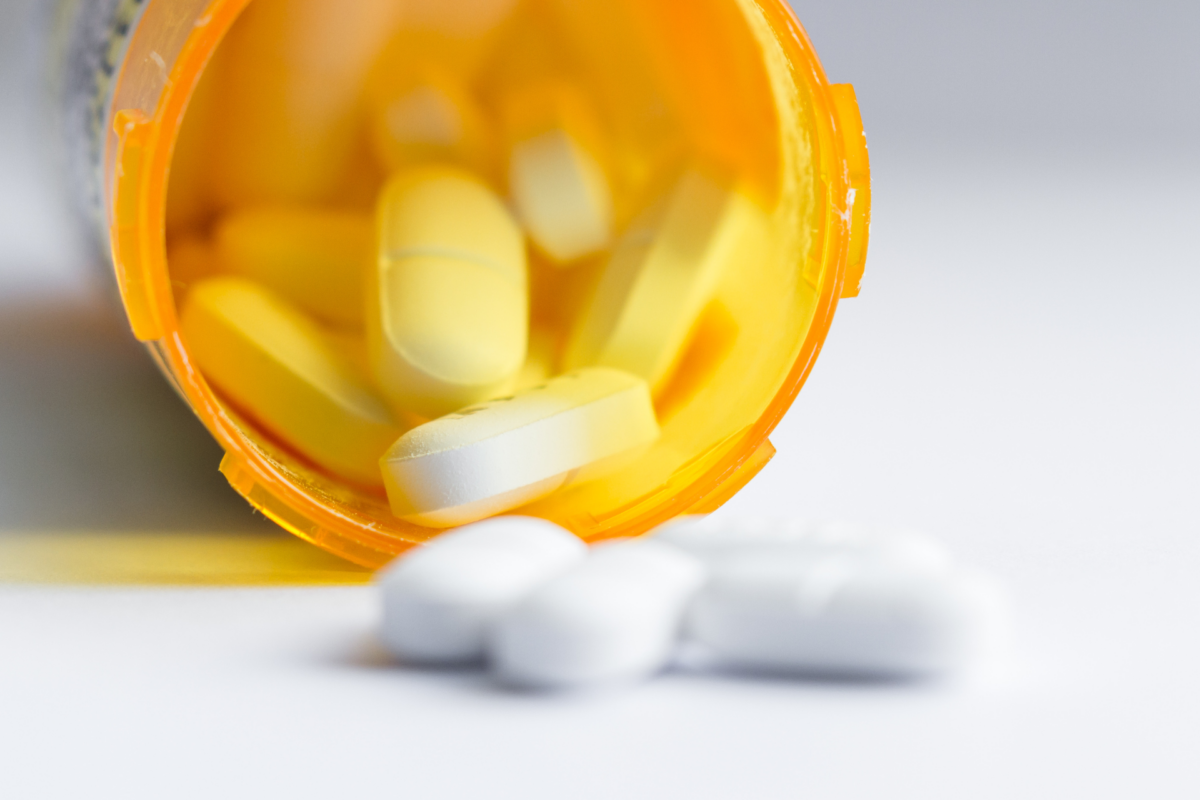 An orange bottle placed horizontally out of which white pills come out.