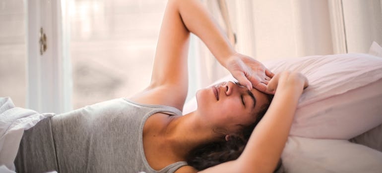 Woman lying in bed and holding her head in pain.