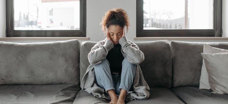 Woman sitting on the couch and holding her temples wondering can alcoholism cause chronic headaches