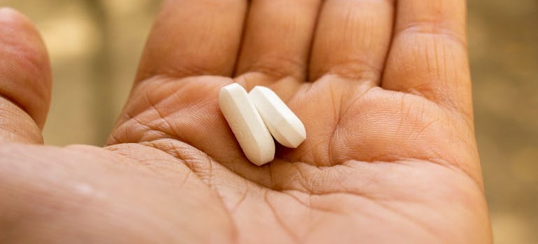 Person holding 2 white pills on their palm.