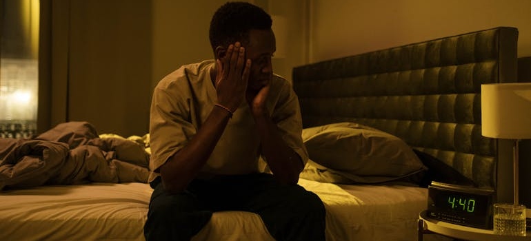 Man sitting on the bed and looking at the clock.