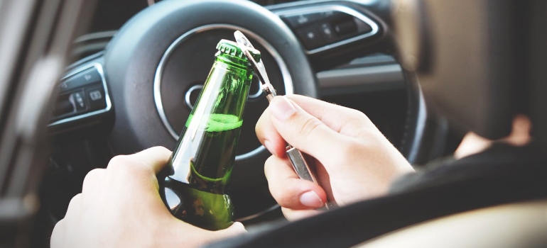 a man in the car opening a bottle of beer 