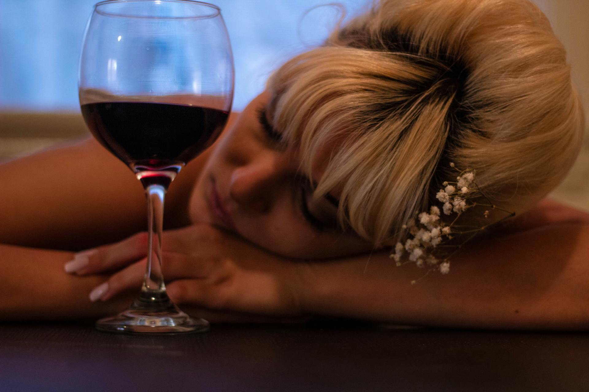 a girl sleeping next to a glass of wine and thinking about Does Alcohol Addiction Run in Families