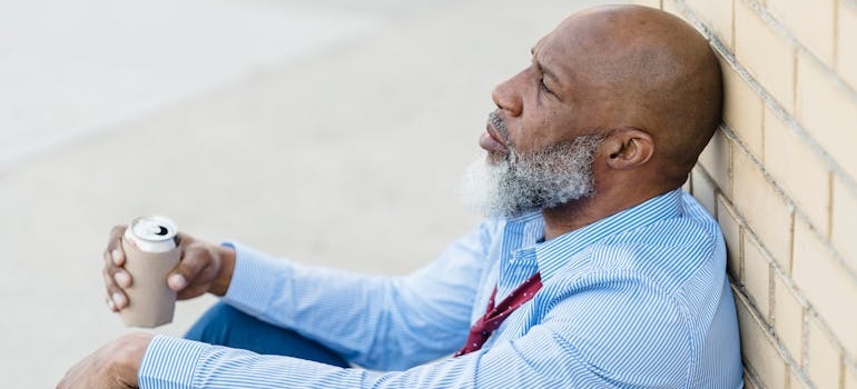 Man leaning against a wall and drinking beer wondering can you drink rubbing alcohol 