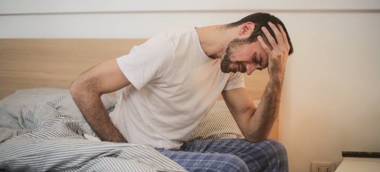 Man sitting on a bed and holding his head in pain.