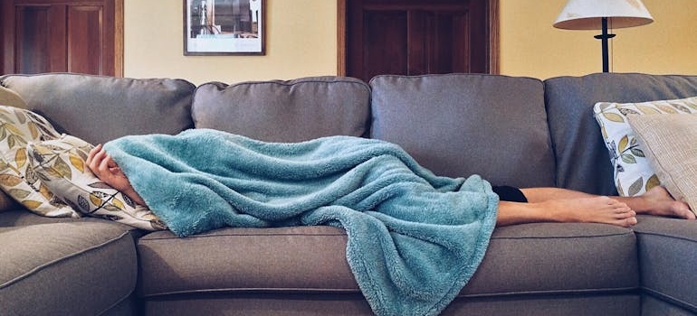 Person lying on the couch covered by a blanket wondering what addiction is the hardest to overcome