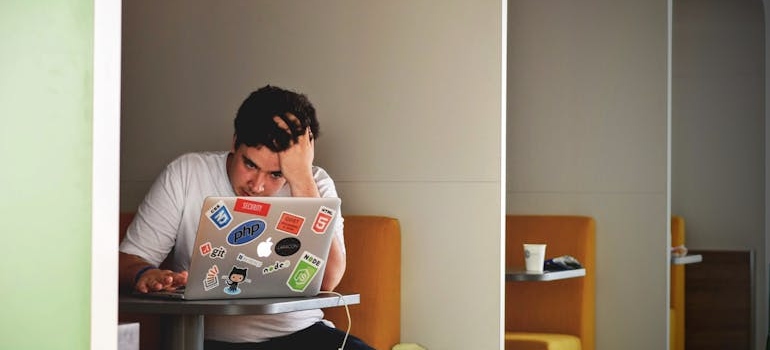 Man sitting in a booth looking at his laptop and holding his head reading about what is ketamine