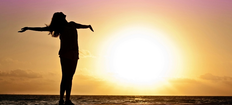 A happy woman is raising her hands on the sunset.