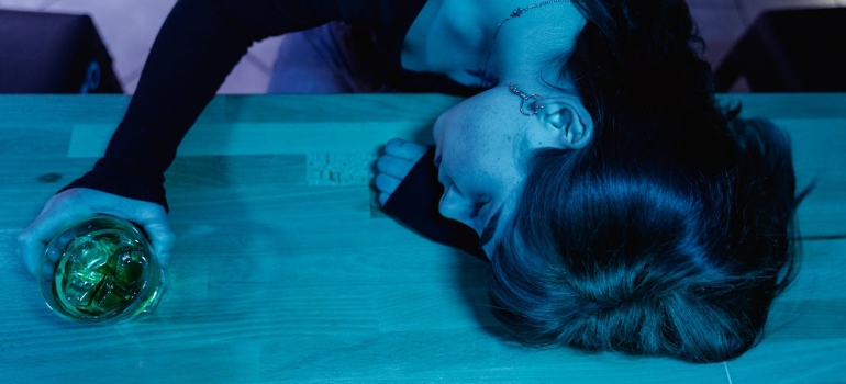 a drunk girl holding a glass and sleeping on the table